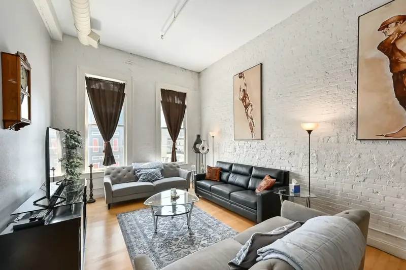 A living room with painted cream city brick walls, two leather sofas and tall windows