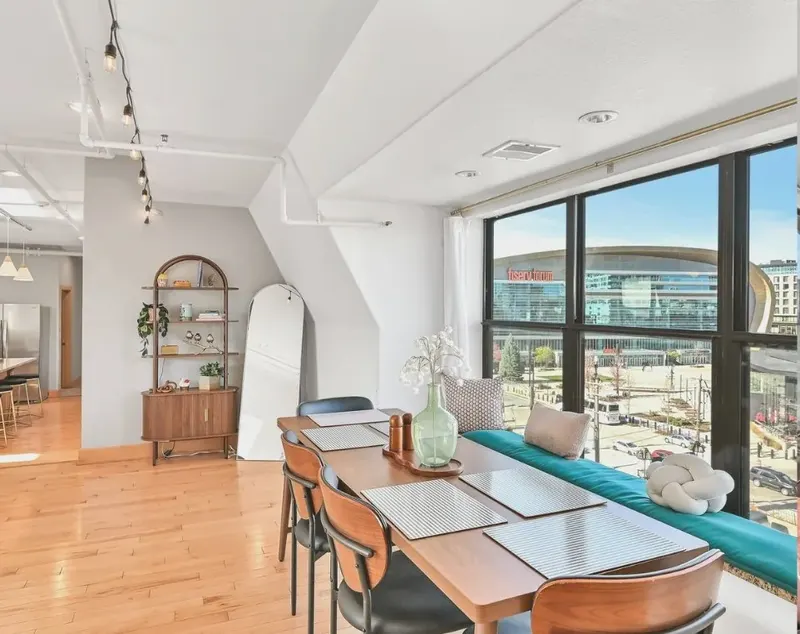 A long dining table set for eight by a wall of windows, with Fiserv Forum across the street