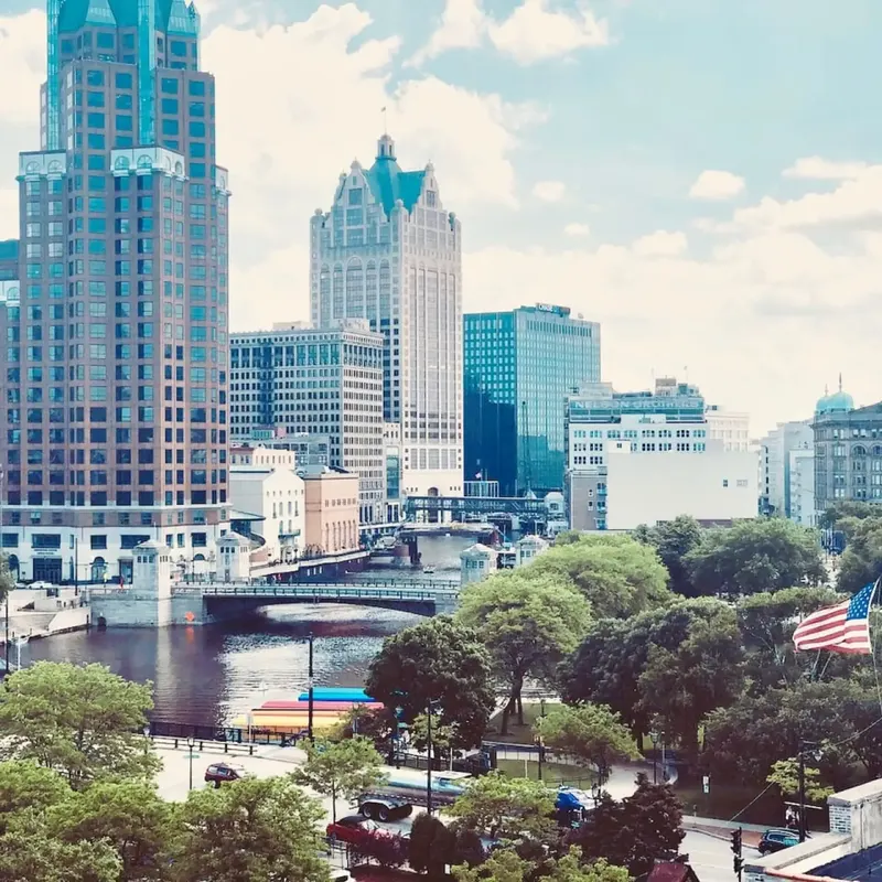 The downtown Milwaukee skyline over the Milwaukee River, with trees along the bank